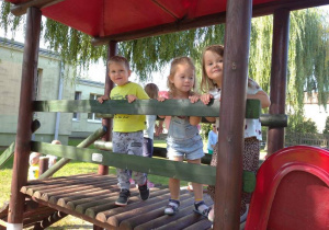 Troje dzieci bawi się w ogrodzie w drewnianym domku.
